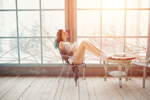 Young woman reading book sitting near window