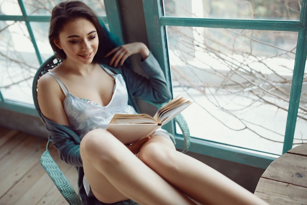 Young woman reading book sitting near window