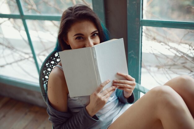 Young woman reading book sitting near window