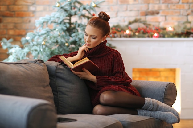 Giovane donna che legge un libro nel divano