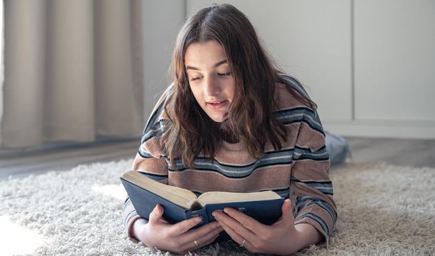 家の床に横になって本を読んでいる若い女性