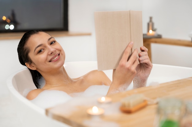 Free photo young woman reading a book while taking a bath