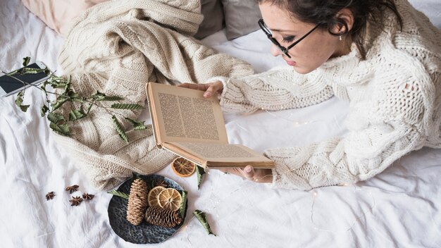 Молодая женщина, чтение книги на белом одеяло