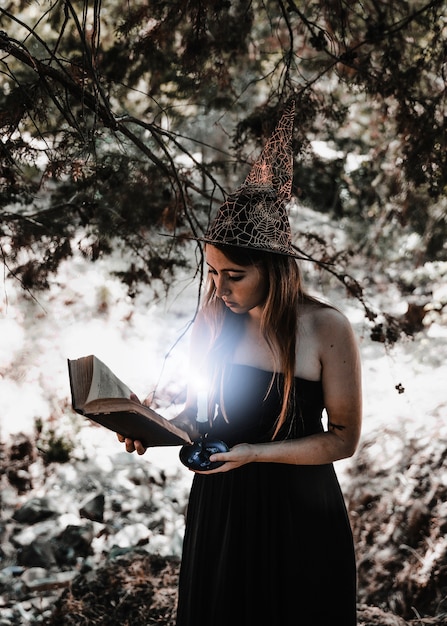 Libro di lettura della giovane donna con la candela bruciante in foresta