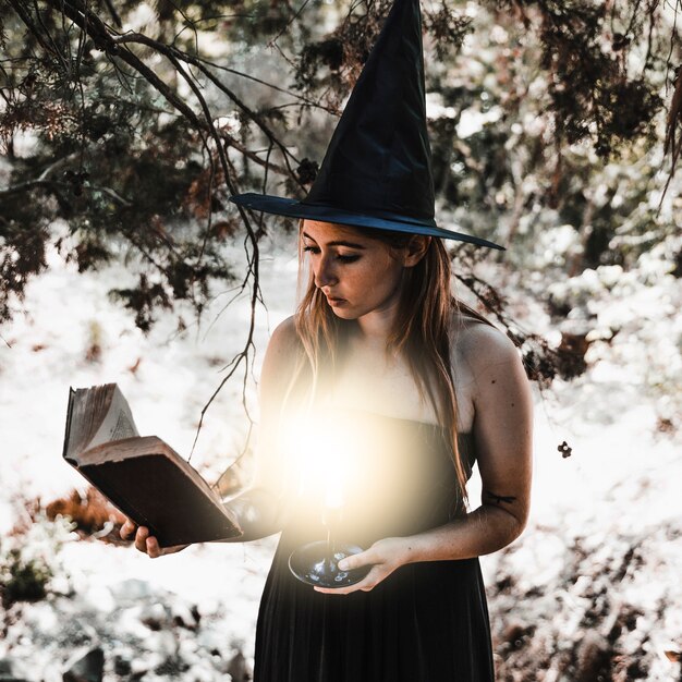 Young woman reading book with burning candle in woods