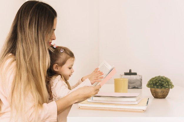 Young woman reading book with daughter at table