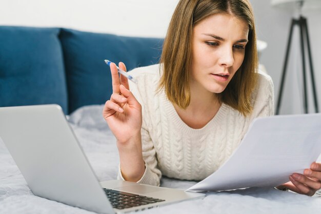 Young woman reading documents on bed