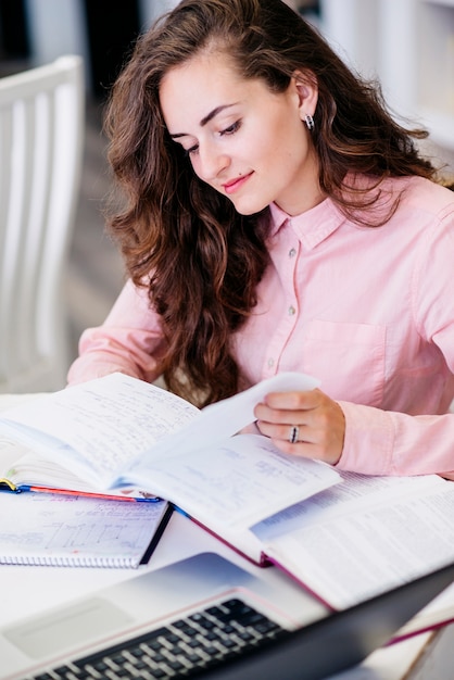 Young woman reading notes at table with laptop