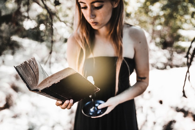 Young woman reading old book with candle in woods