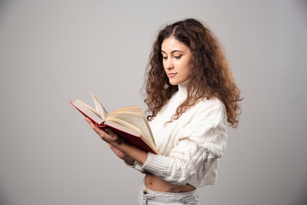 Young woman reading a red book on a gray wall. High quality photo