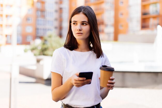Молодая женщина, чтение с помощью телефона. Женские новости чтения женщины или отправляя СМС sms на smartphone пока выпивающ кофе на проломе от работы.