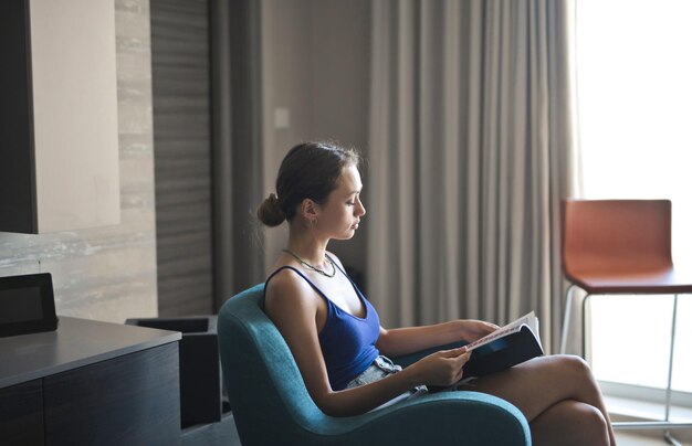 young woman reads a magazine sitting on an armchair in her home