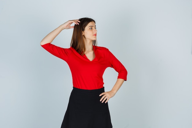 Young woman in red blouse, black skirt holding one hand on head