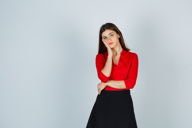 Young woman in red blouse, black skirt leaning cheek on palm