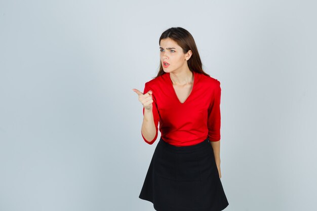 Young woman in red blouse, black skirt pointing with index finger