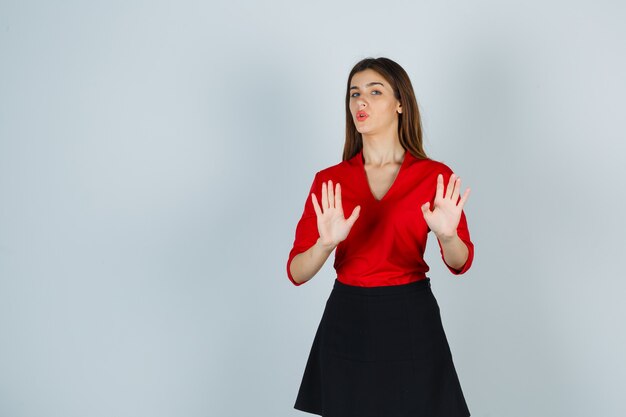 Young woman in red blouse, black skirt showing restriction gesture and looking cute