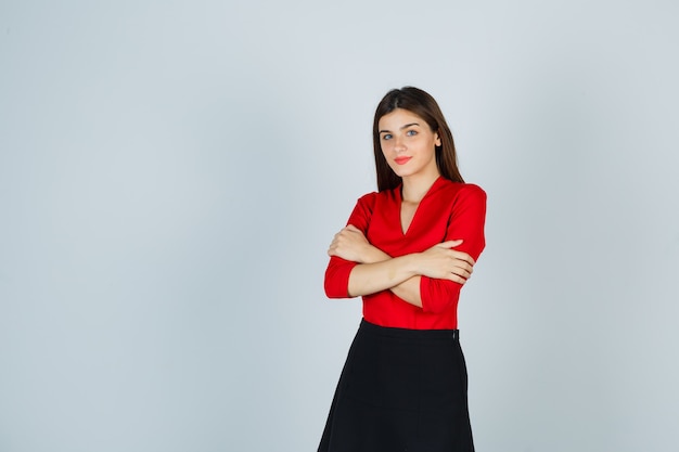 Young woman in red blouse, black skirt standing arms crossed and looking cheery