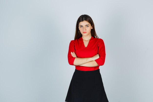 Young woman in red blouse, black skirt standing arms crossed and looking confident