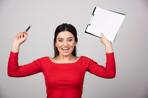 Young woman in red blouse with clipboard feeling happy.