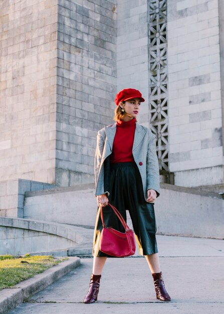 Young woman in red cap holding bag standing in front of building