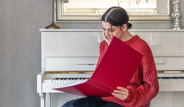 A young woman in a red knitted sweater near a white piano