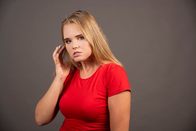 Young woman in red shirt posing on black wall.