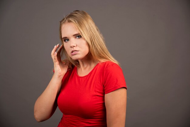 黒い壁にポーズをとって赤いシャツを着た若い女性。