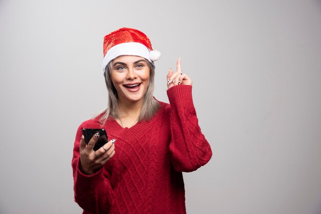 灰色の背景に携帯電話を保持している赤いセーターの若い女性。