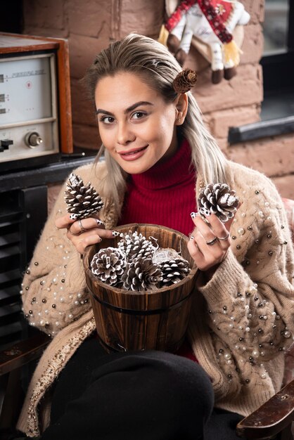 Young woman in red sweater holding a wooden basket full of pinecones