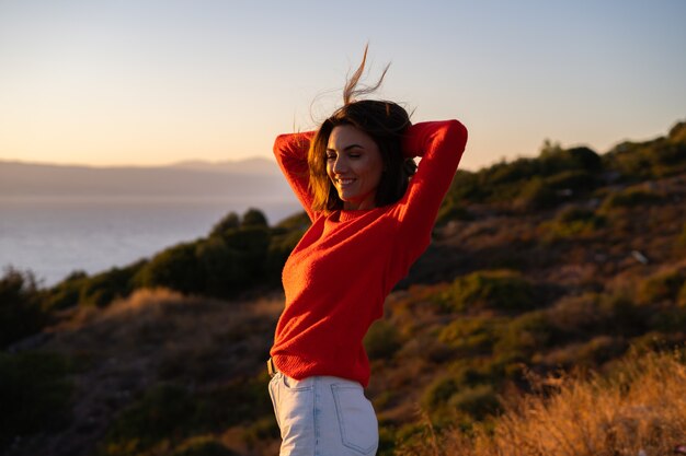산의 장엄한 일몰에 빨간 스웨터를 입은 젊은 여자