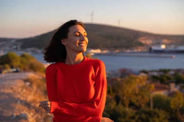 山の壮大な夕日に赤いセーターを着た若い女性