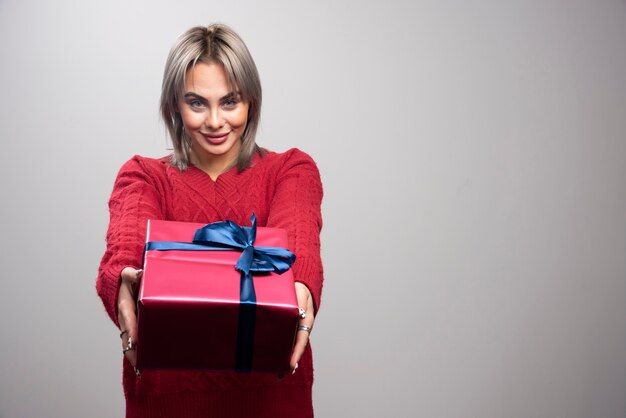 Young woman in red sweater offering Christmas gift.