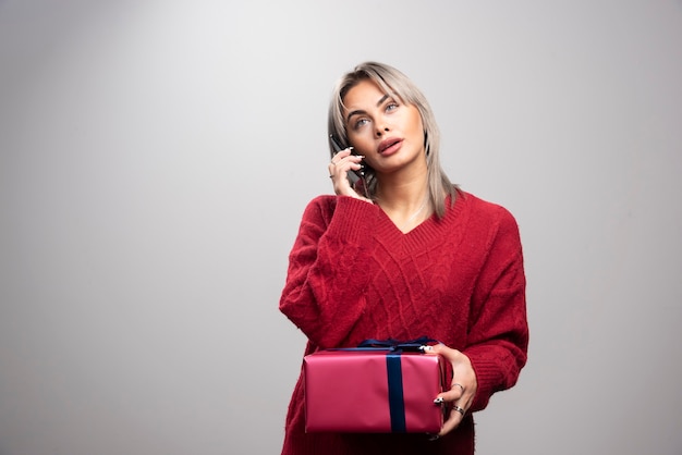 핸드폰에 얘기 하는 빨간 스웨터에 젊은 여자.