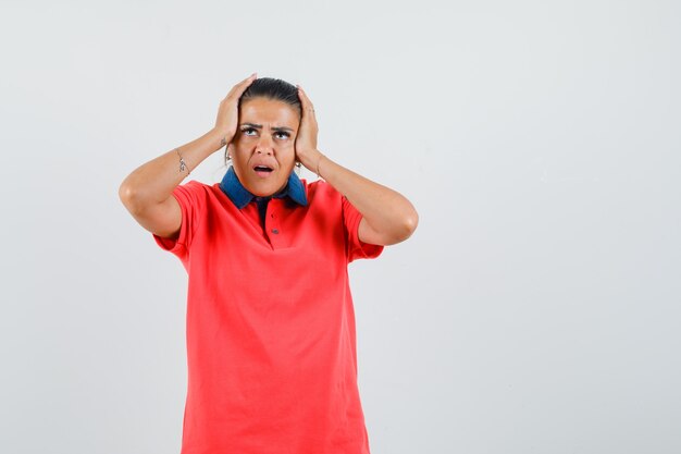 Young woman in red t-shirt putting hands on head and looking annoyed , front view.