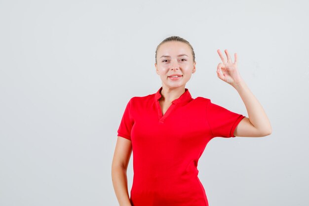 Young woman in red t-shirt showing ok gesture and looking happy