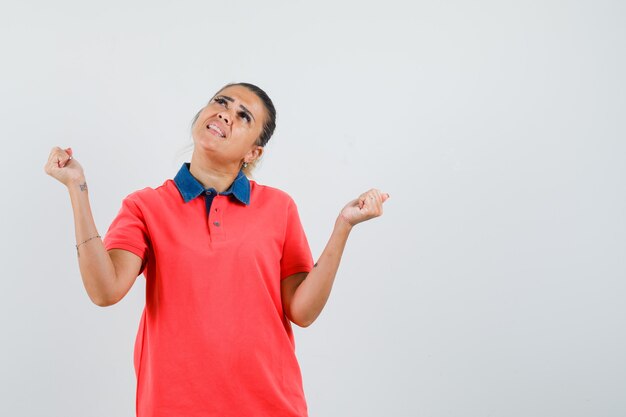 Young woman in red t-shirt showing success gesture and looking happy , front view.