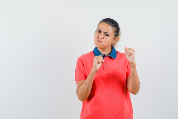 ボクサーのポーズで立って頬を膨らませて、力強く見える赤いTシャツの若い女性、正面図。