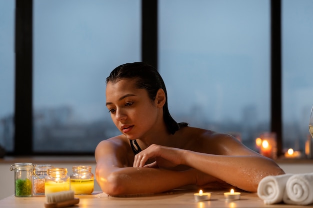 Молодая женщина расслабляется и смотрит на свечи, принимая ванну