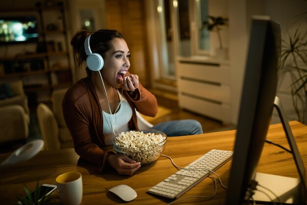 컴퓨터로 영화를 보고 집에서 팝콘을 먹으면서 밤에 휴식을 취하는 젊은 여성