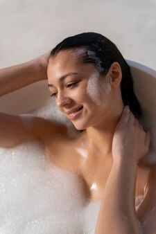 Giovane donna che si rilassa e fa il bagno in una vasca da bagno piena di acqua e schiuma