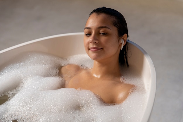 Молодая женщина расслабляется и принимает ванну в ванне, наполненной водой и пеной