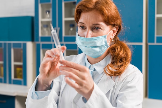 Free photo young woman researcher with mask and syringe