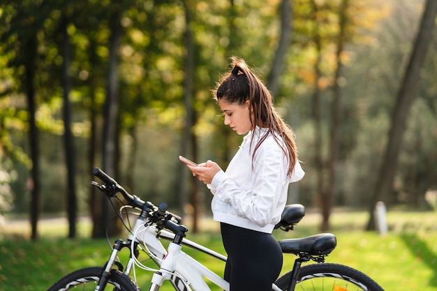 公園で休んでいる若い女性は、晴れた天気で携帯電話を使用しています