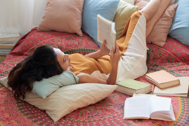 베개에 그녀의 다리와 함께 침대에서 책을 쉬고 젊은 여자