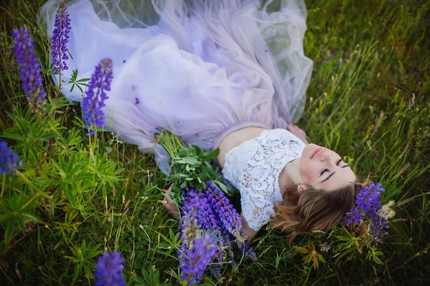 Young woman in rich dress lies with bouquet of violet flowers on green field 