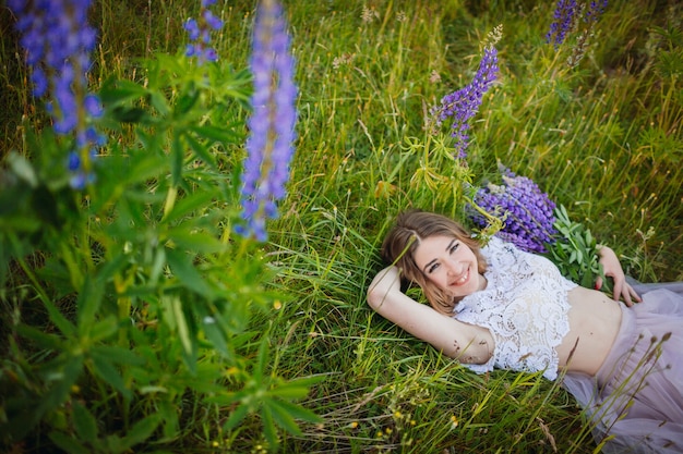 Young woman in rich dress lies with bouquet of violet flowers on green field 
