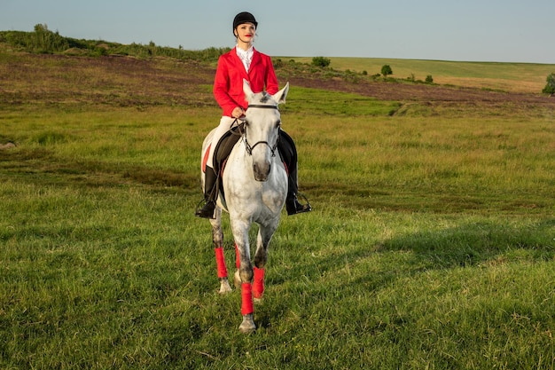 Free photo young woman rider, wearing red redingote and white breeches, with her horse in evening sunset light. outdoor photography in lifestyle mood