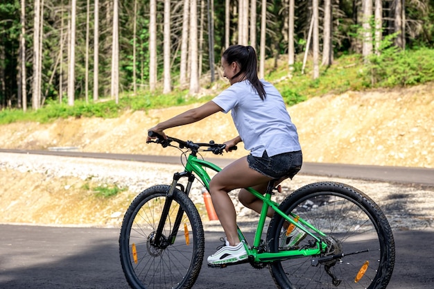 A young woman rides a bicycle in a mountainous area in the forest