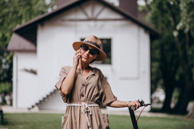 Young woman riding scooter and talking on phone in park