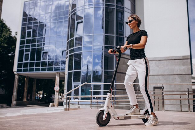 Young woman riding scotter by the skyscraper